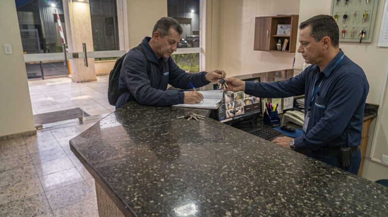 Dois porteiros no balcão passando o livro de ocorrências na troca de turno